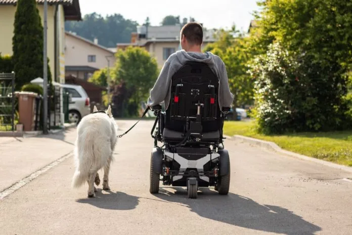 Invalid na električnem invalidskem vozičku v spremstvu psa pomočnika.