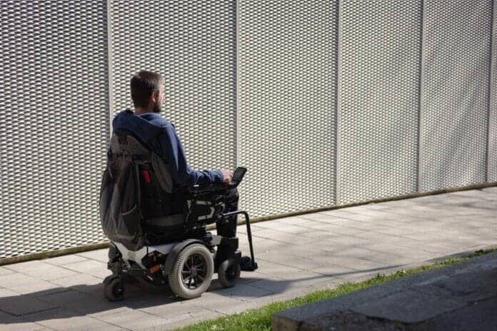 Invalid na električnem invalidskem vozičku se pelje po betonski podlagi ob zidu.